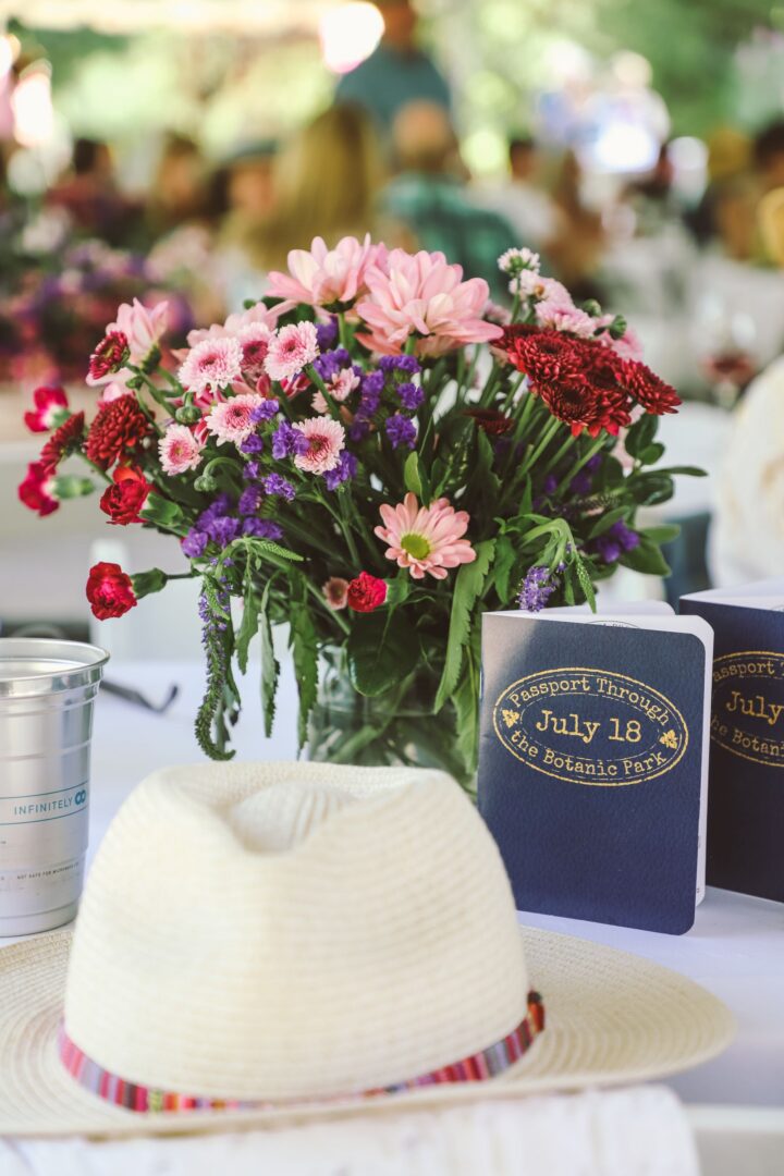 Flowers and hat next to a passport book that reads "Passport Through the Botanic Park July 18"