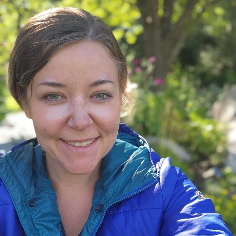 A woman with dark hair and a blue rain coat smiling