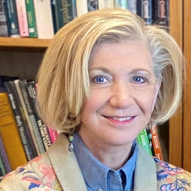 A woman with blond hair smiles against a background with full bookshelves
