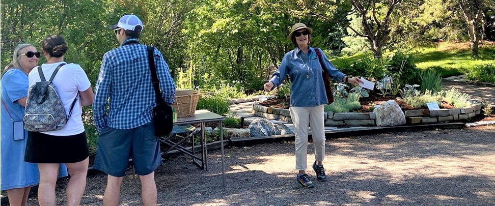 A tour guide enthusiastically motions a group of visitors over to her to continue their tour of the gardens