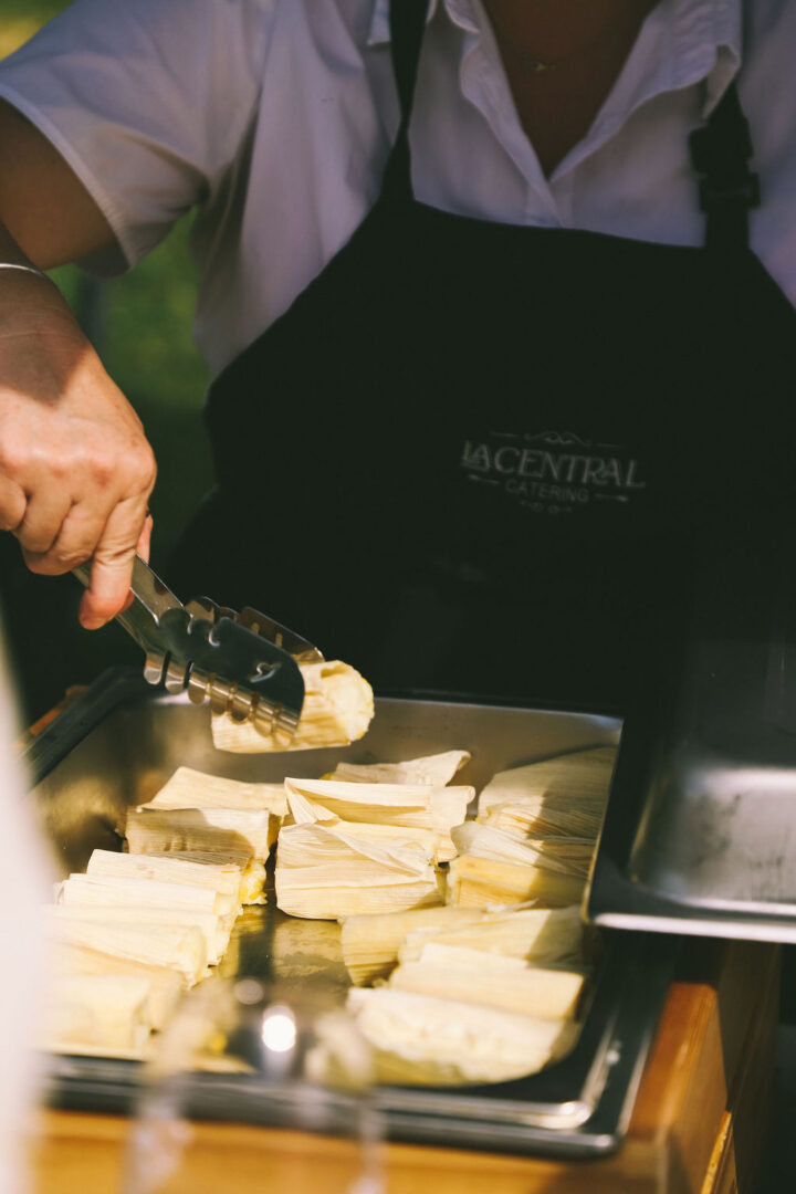 La Central caterer picking up a cheese humitas with tongs