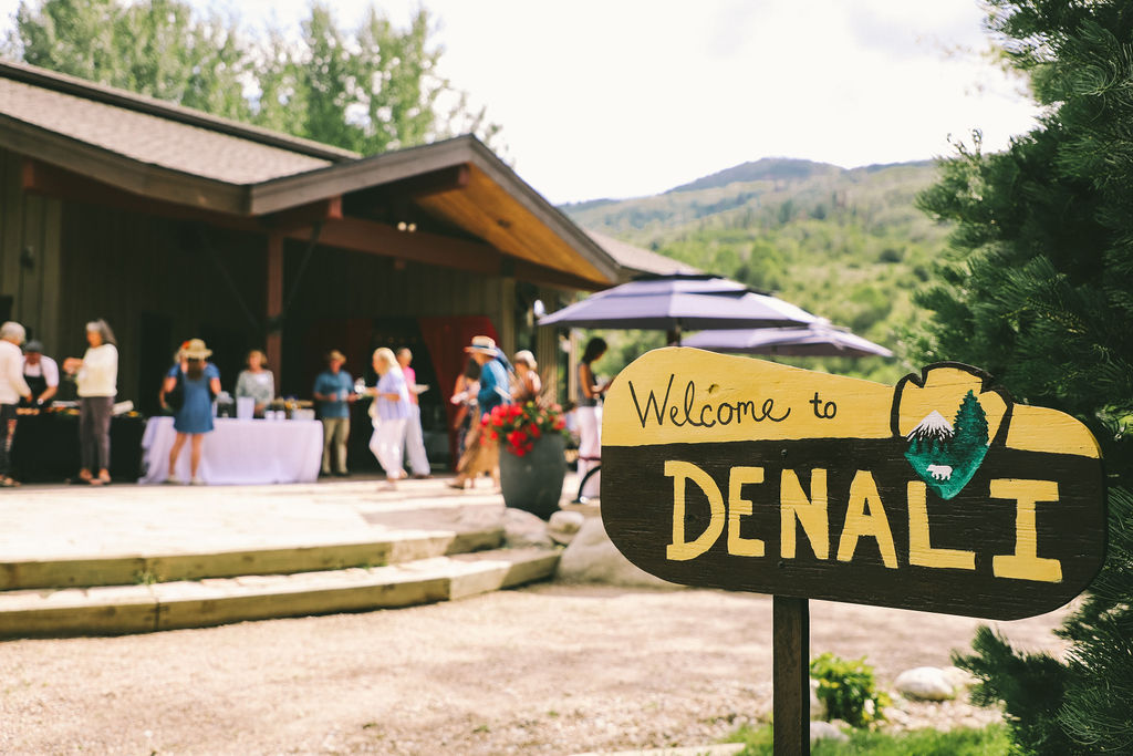 Sign that reads "Welcome to Denali" with people mingling in the background