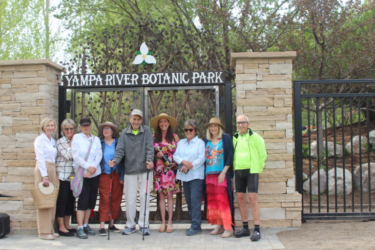 Group of people posing happily in front of the Yampa River Botanic Park gate on a sunny day.