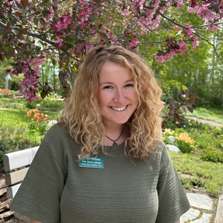 Woman with curly blond hair wearing a green knit sweater with purple flowers hanging above her