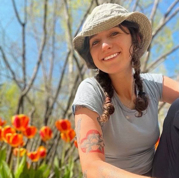 A woman with dark braided hair sits on the ground next to orange tulips