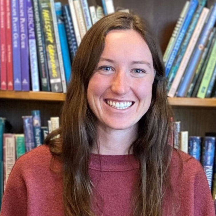 A woman with dark hair smiles against a background with full bookshelves