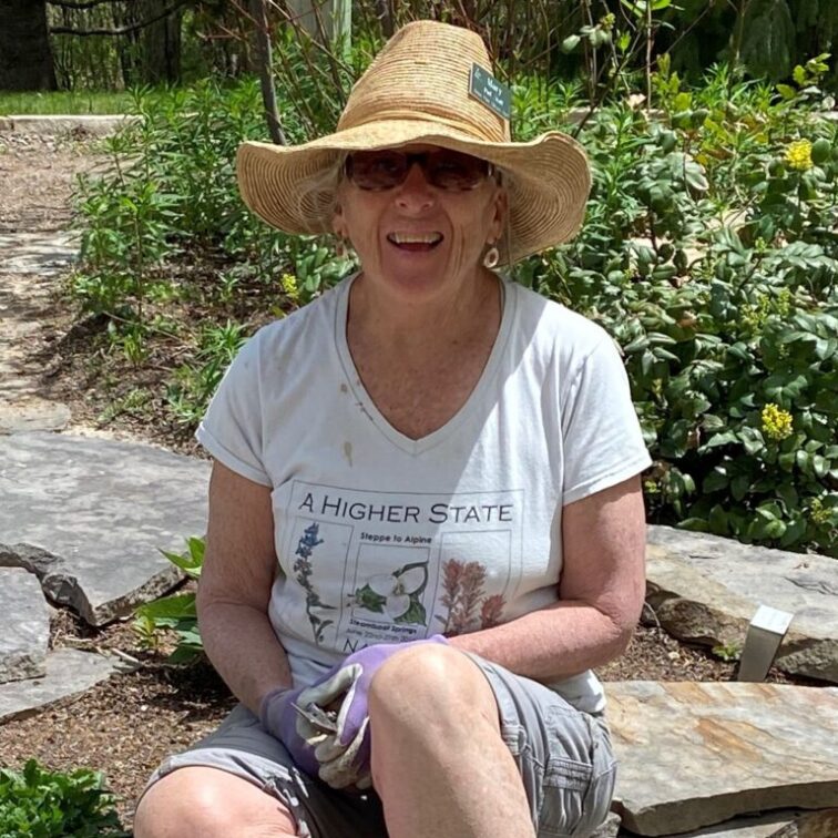 A woman in a sunhat sits on the ground near a bed of wildflowers