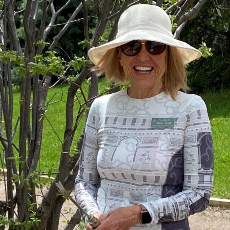 A woman in a white shirt stands smiling next to a tree