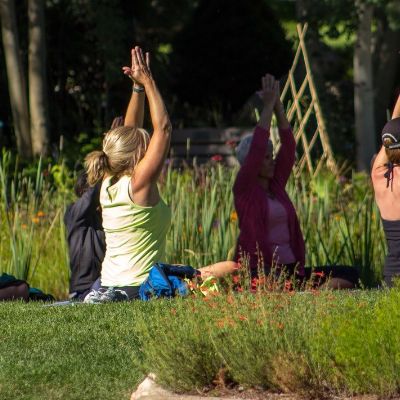 Five women sitting in grass performing stretching exercises.