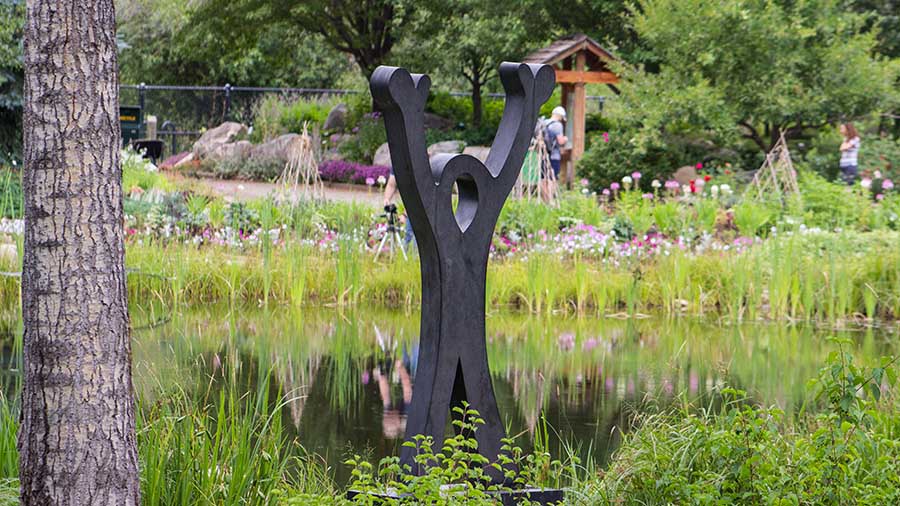 An abstract metal sculpture resembling a stick figure with its arms raised high above the head