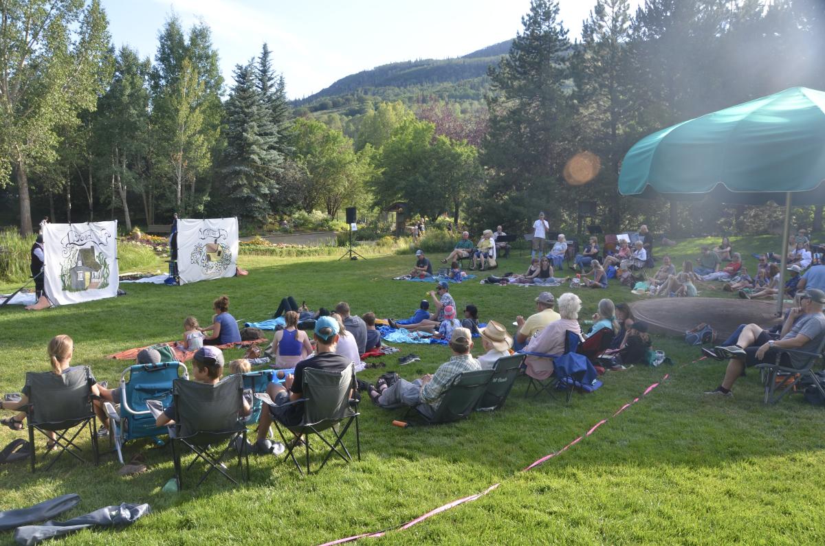 People sitting in lawn chairs watching an outdoor play in a park